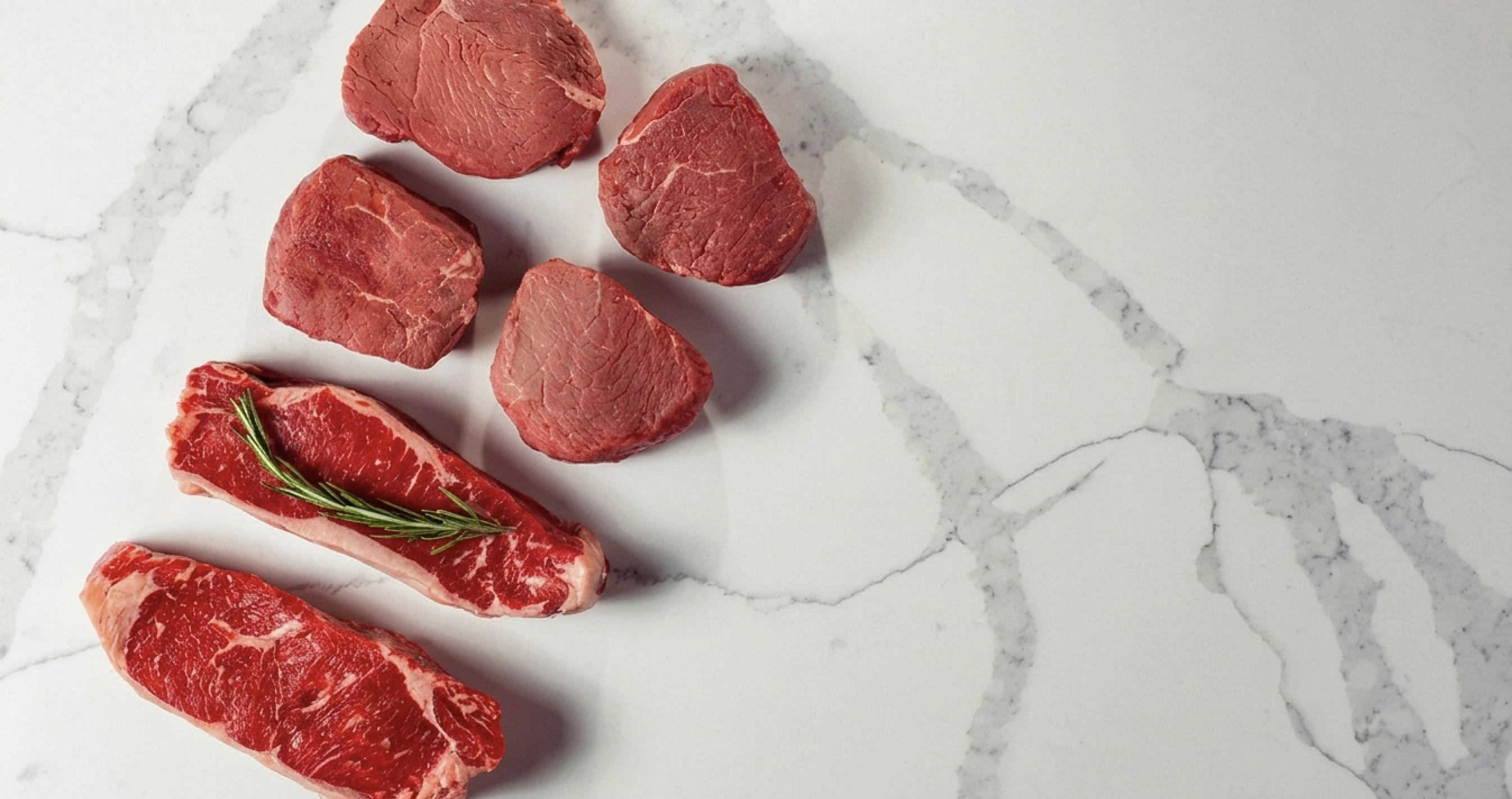 Premium steaks, pork chops, and seafood plated on white marble